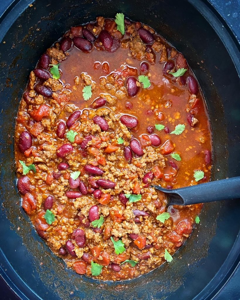 overhead shot of cooked beef chili in a black slow cooker garnished with fresh cilantro