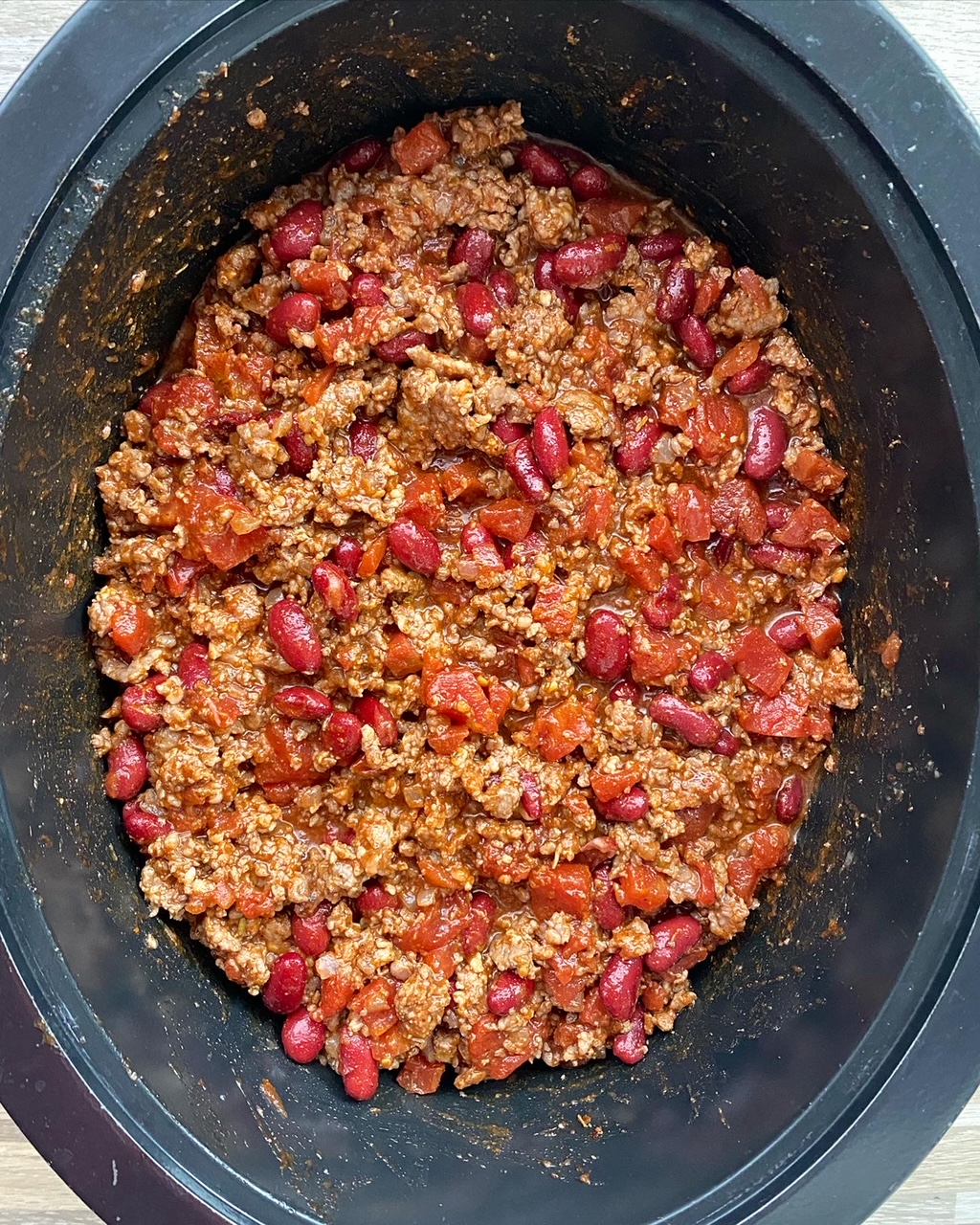 overhead shot of uncooked beef chili in a black slow cooker