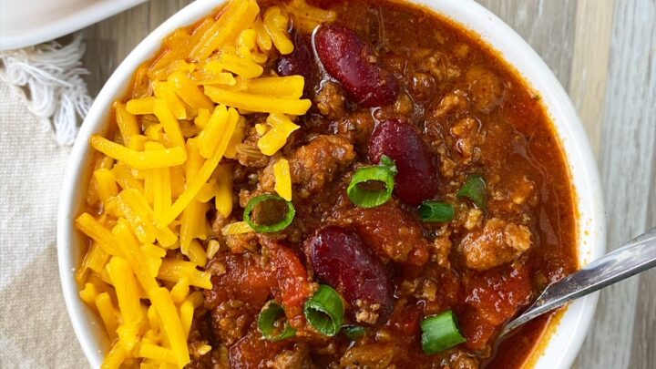 overhead shot of chili in a bowl garnished with green onion and cheese with cornbread on the side
