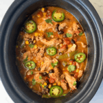 overhead shot of cooked Santa Fe Chicken in a black crockpot garnished with sliced jalapenos and fresh cilantro