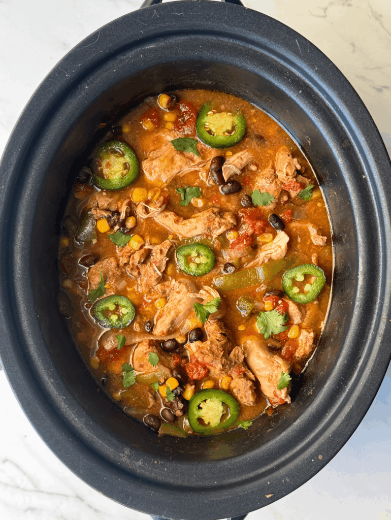 overhead shot of cooked Santa Fe Chicken in a black crockpot garnished with sliced jalapenos and fresh cilantro