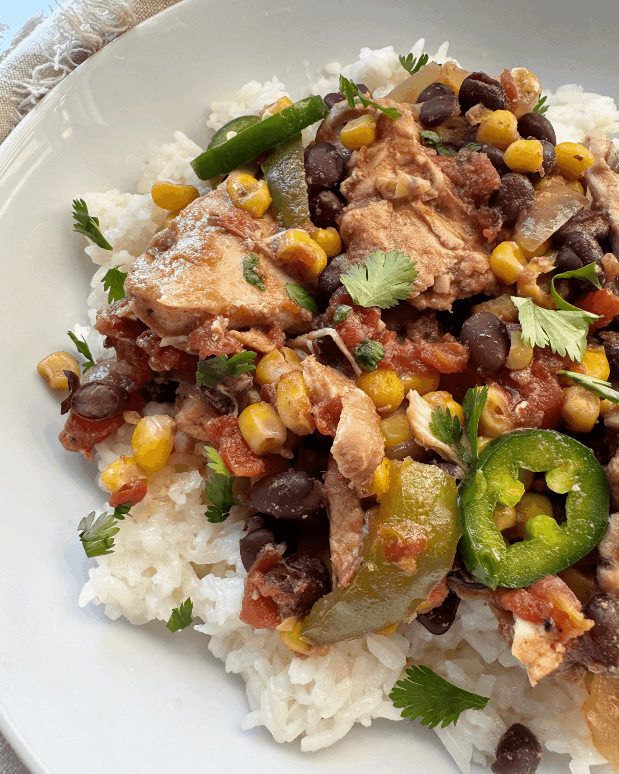 close up shot of cooked Santa Fe Chicken on a white plate garnished with sliced jalapenos and fresh cilantro