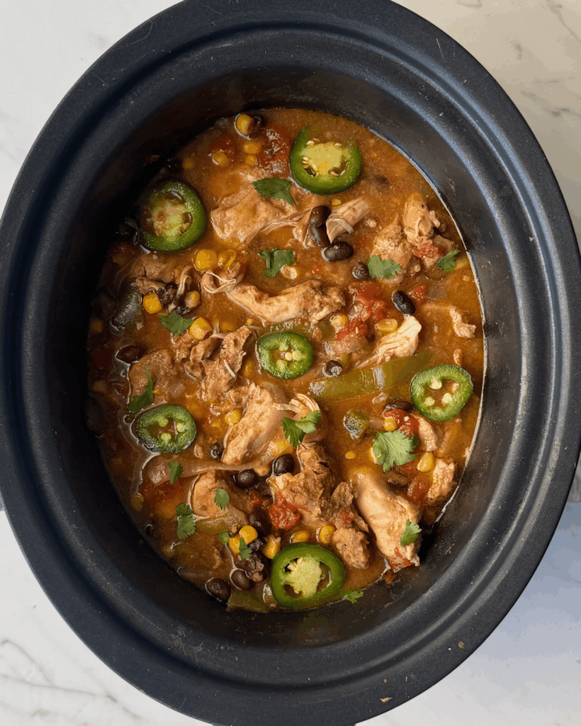 overhead shot of cooked Santa Fe Chicken in a black crockpot garnished with sliced jalapenos and fresh cilantro