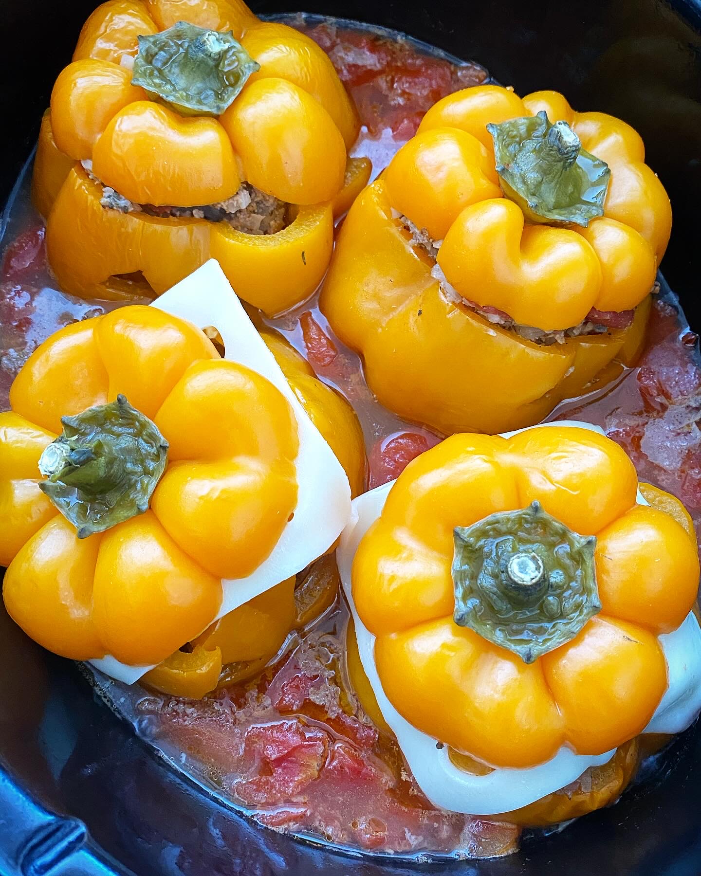 overhead shot of cooked crockpot Halloween jack-o-lantern stuffed peppers with slices of cheese added under 2