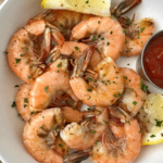 overhead, close up shot of cooked peel and eat shrimp on a white plate with cocktail sauce and lemon