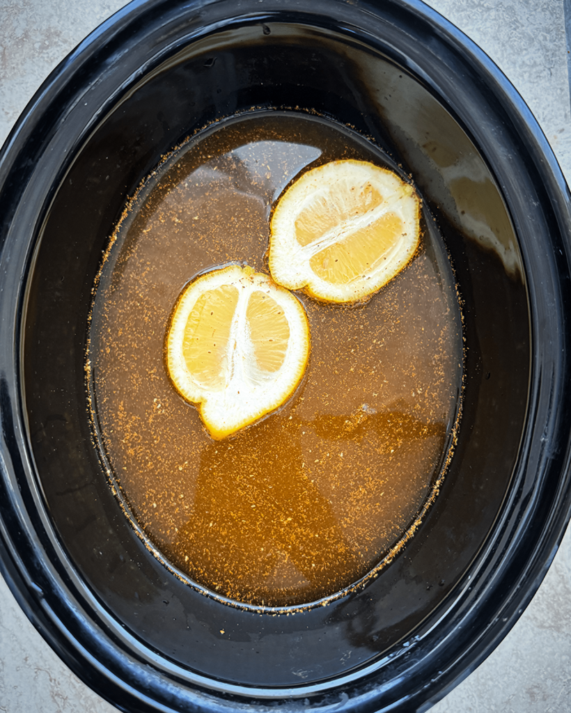 overhead shot of water, old bay, and lemon in a black slow cooker