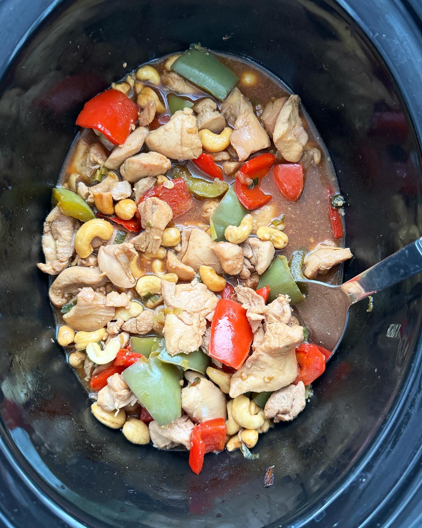 overhead shot of cooked cashew chicken in a black slow cooker