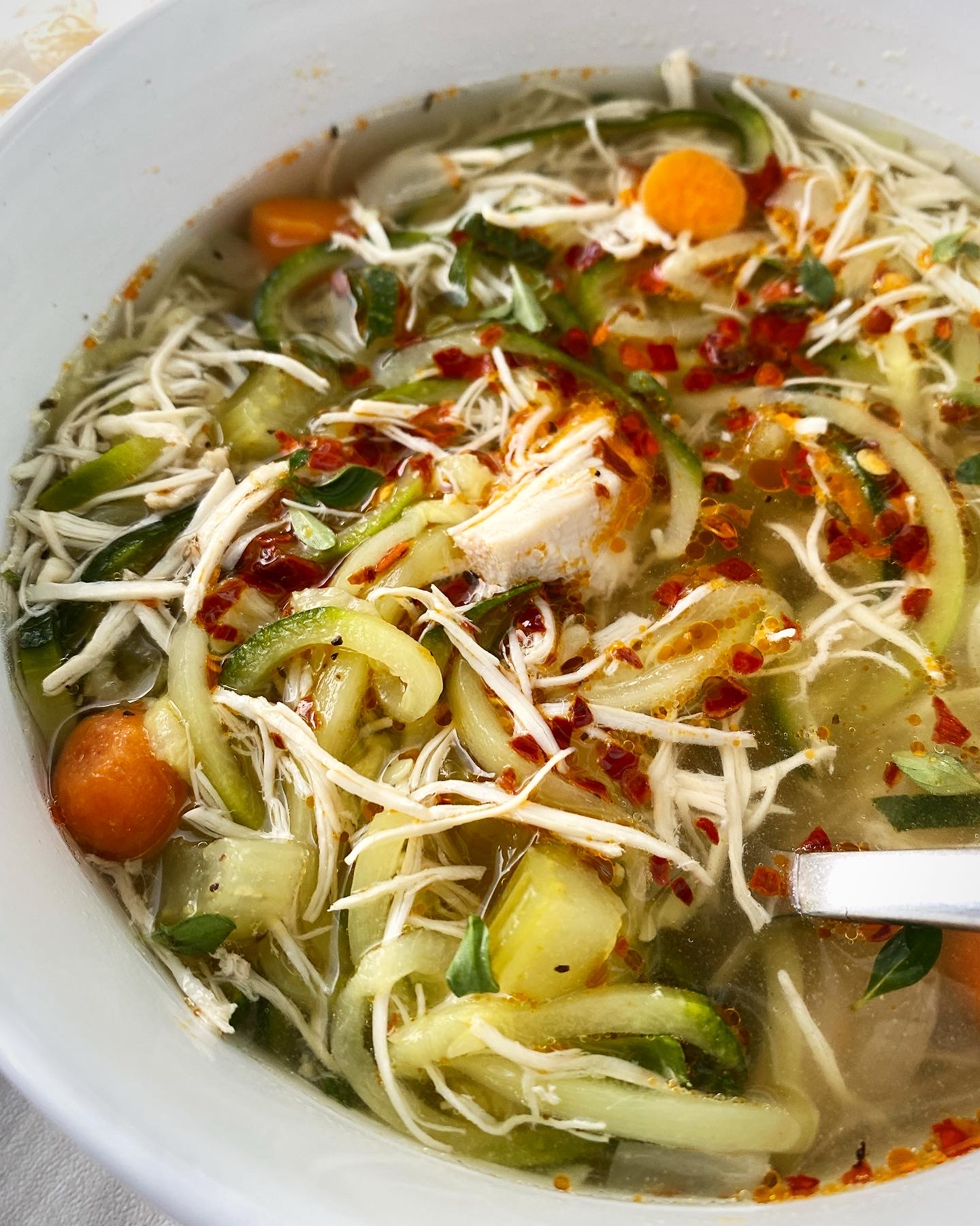 close up, side view shot of slow cooker chicken zoodle soup in a white bowl garnished with chili oil