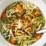 overhead shot of slow cooker chicken zoodle soup in a white bowl garnished with chili oil