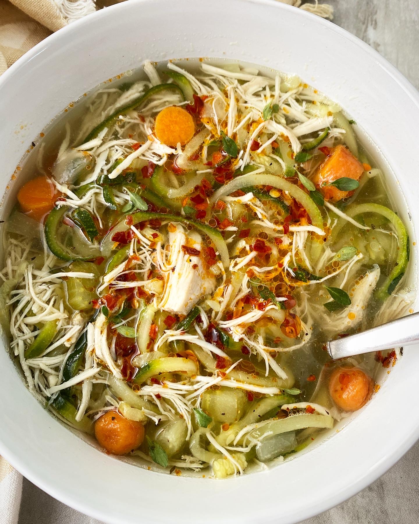 overhead shot of slow cooker chicken zoodle soup in a white bowl garnished with chili oil