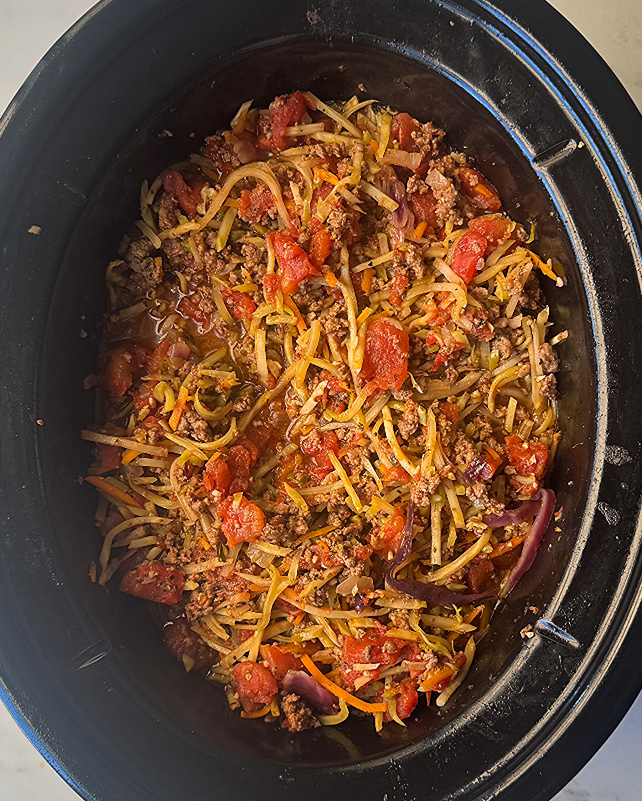 overhead shot of cooked slawghetti in a black slow cooker