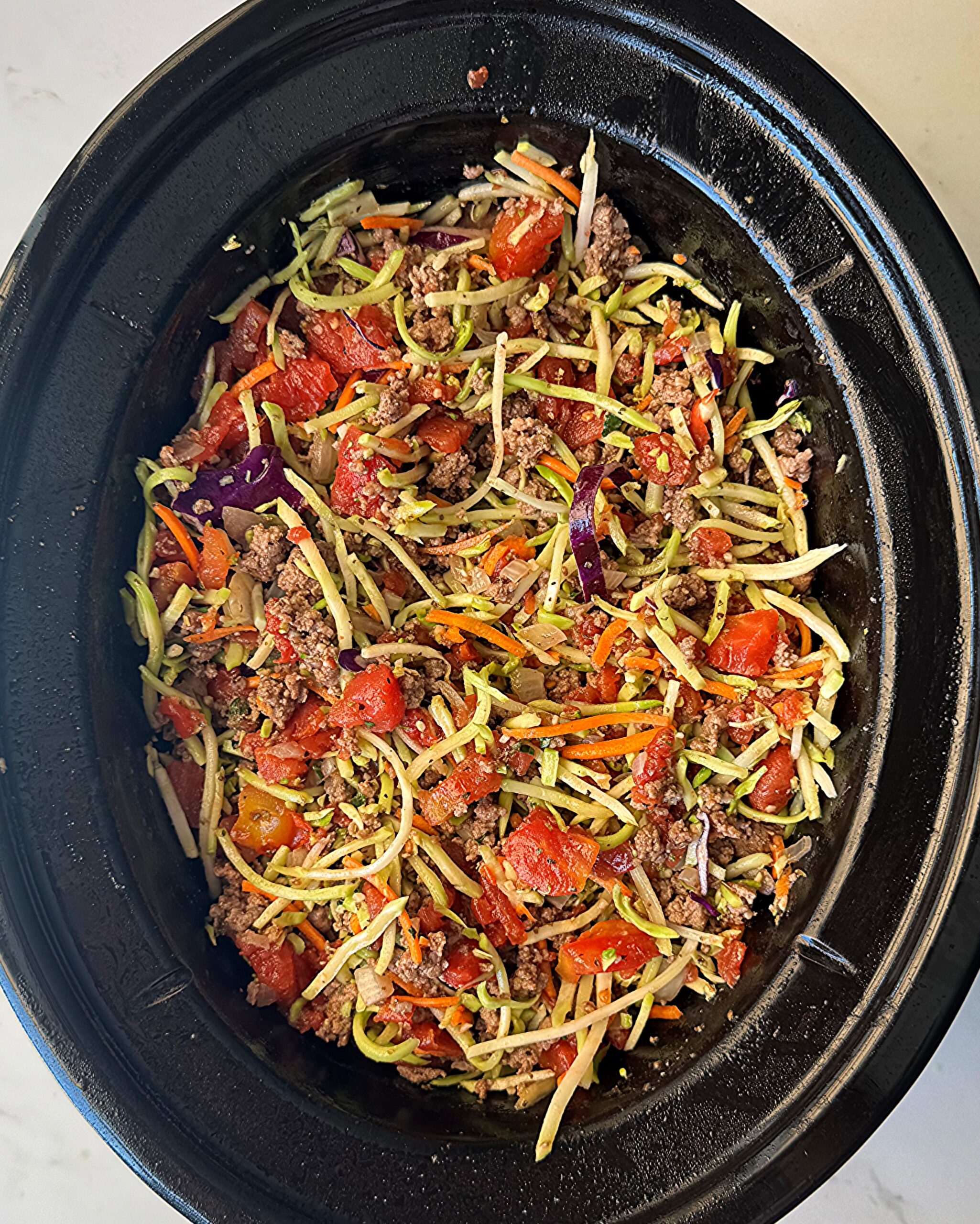 overhead shot of uncooked slawghetti in a black slow cooker