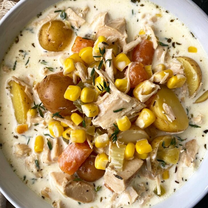 overhead shot of turkey corn chowder in a white bowl garnished with fresh thyme