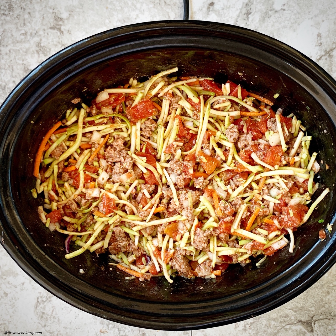 overhead shot of uncooked slawghetti in a black slow cooker