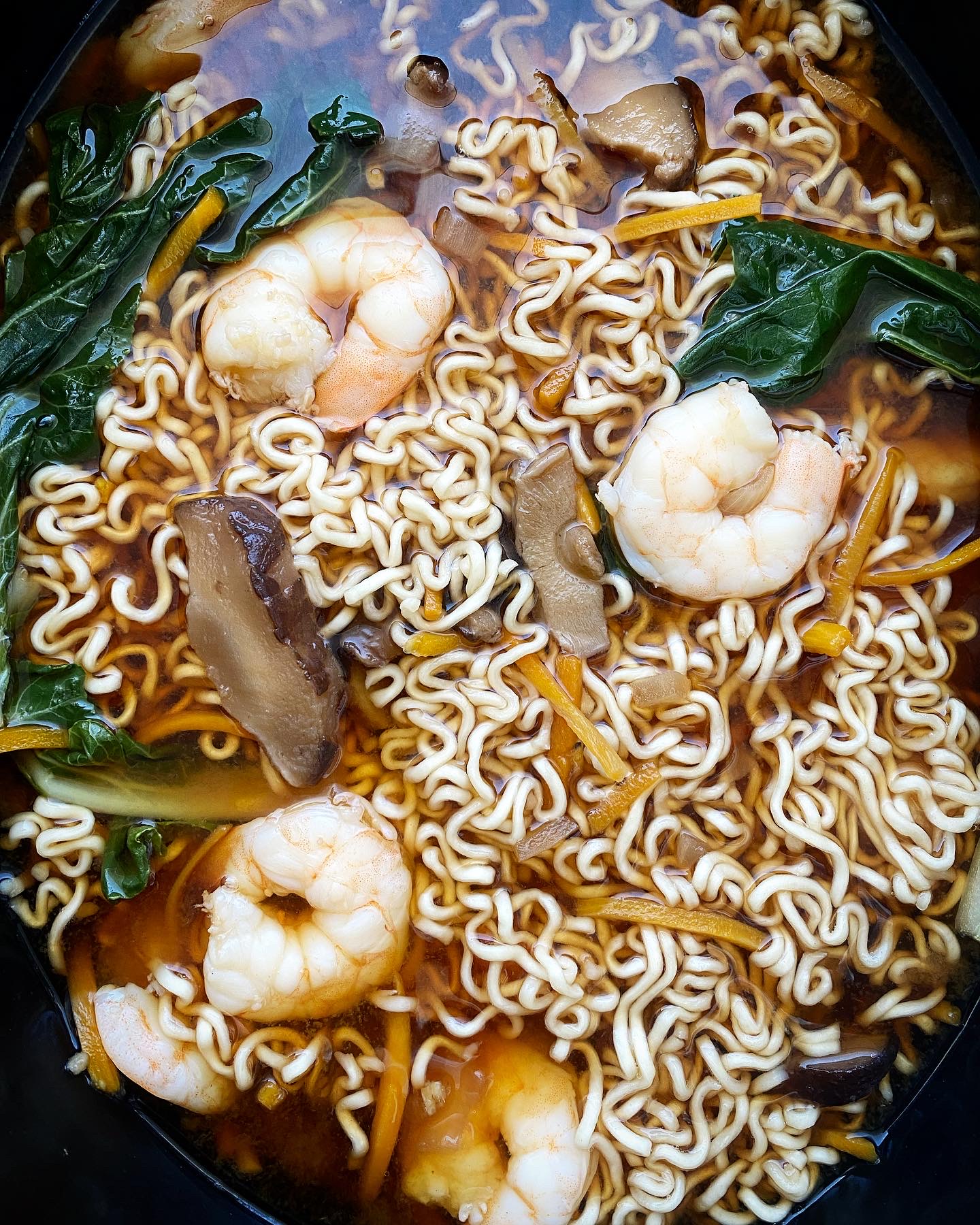 overhead shot of cooked soup with ramen, shrimp, and bok choy in a black slow cooker