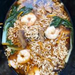 overhead shot of cooked soup with ramen, shrimp, and bok choy in a black slow cooker