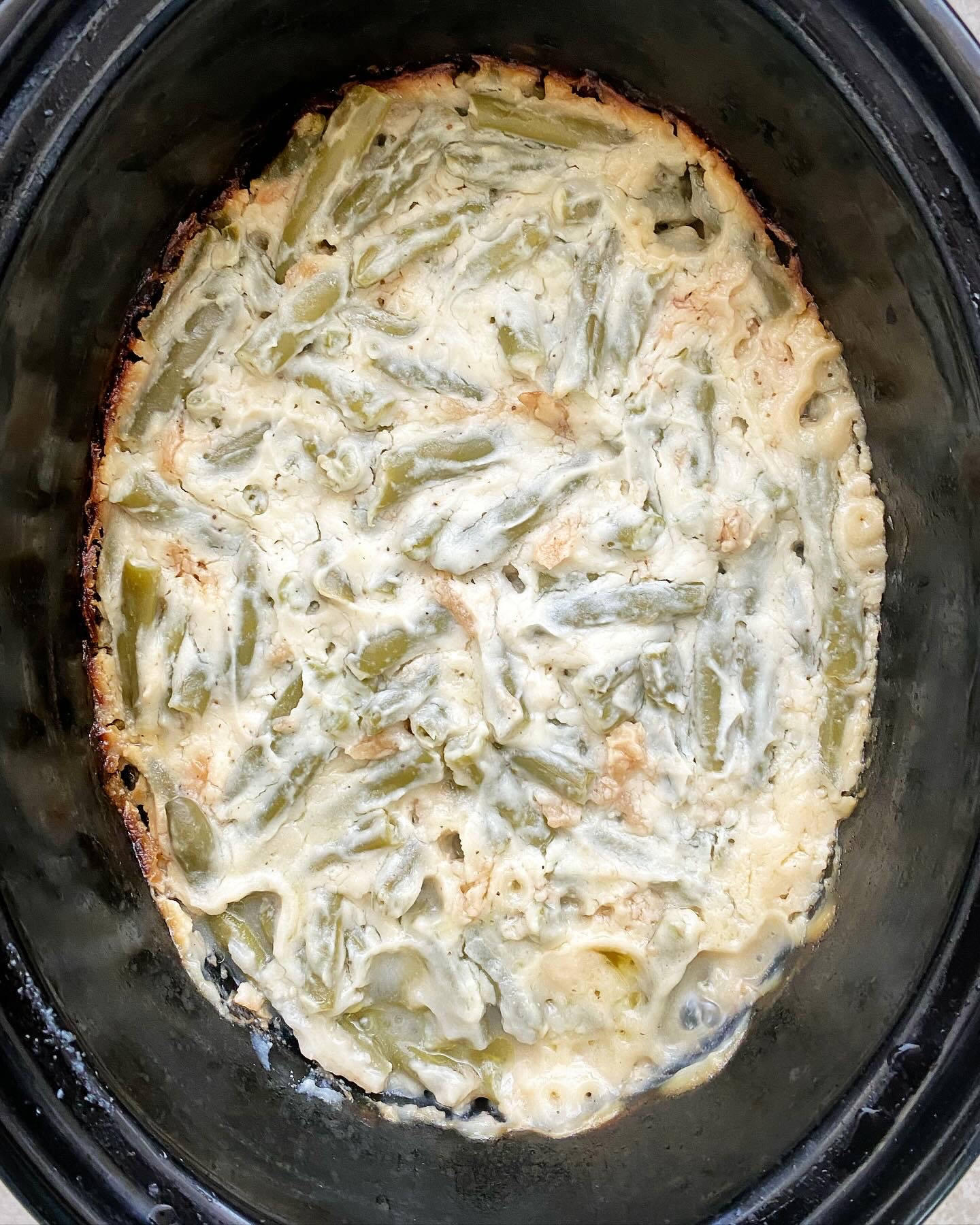 overhead shot of cooked healthy green bean casserole in a black slow cooker