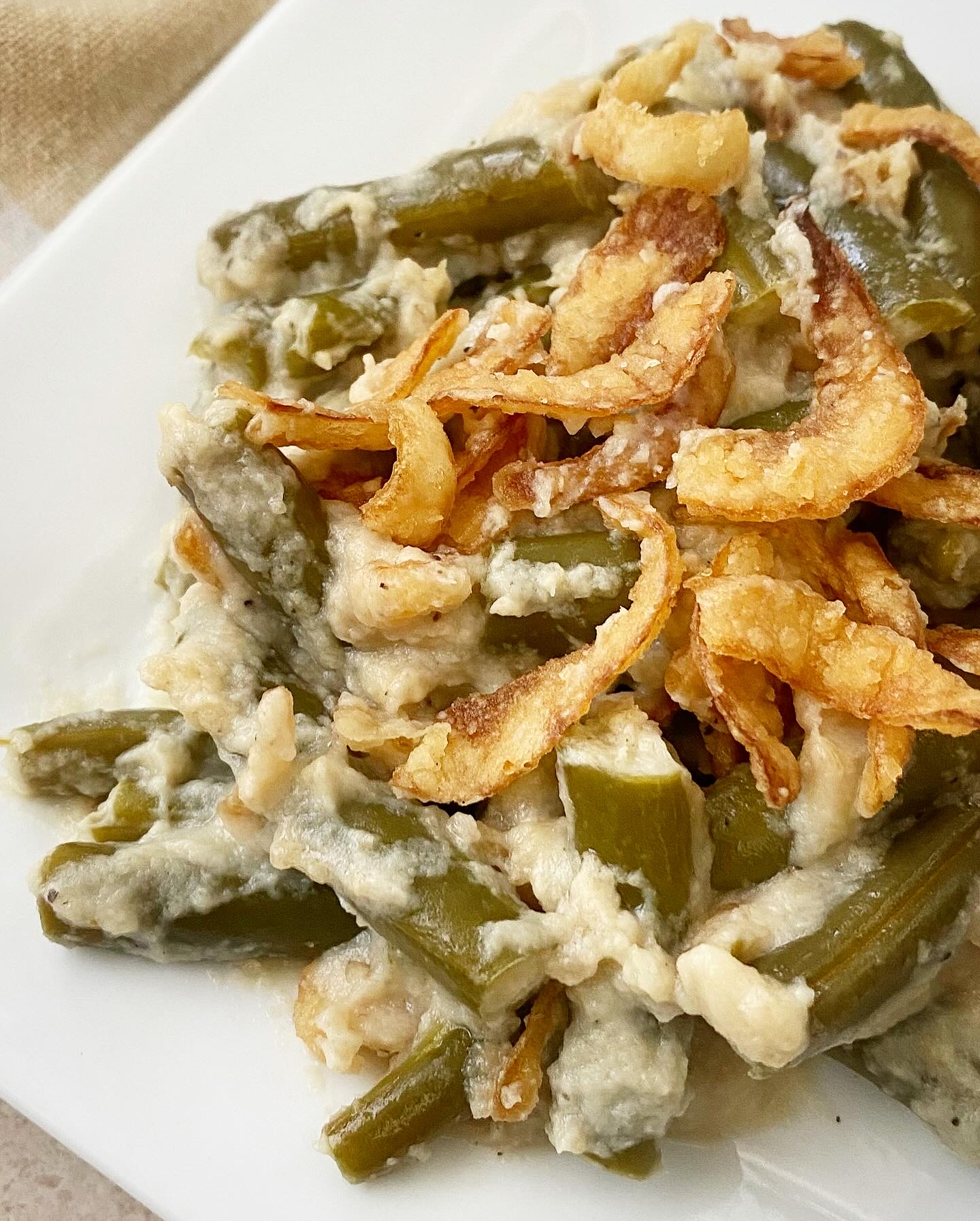close up shot of healthy crockpot green bean casserole on a white plate topped with French fried onions