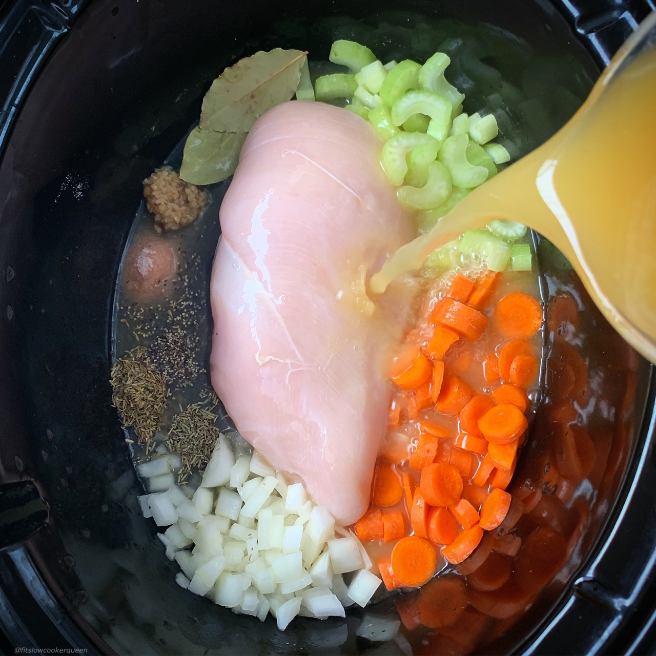 raw chicken, celery, onion, carrots, garlic, bay leaf, and seasonings in the slow cooker with broth being poured in