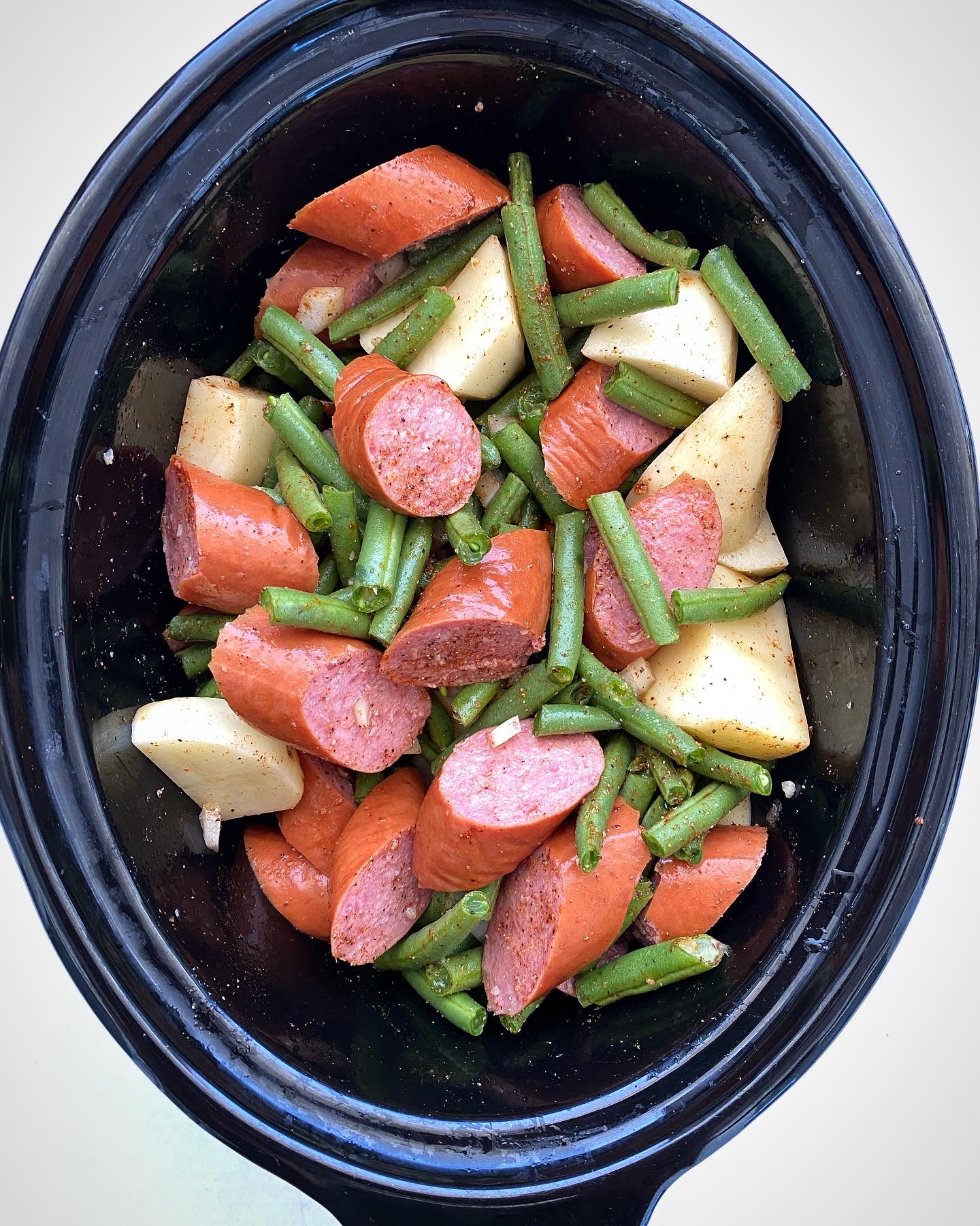 overhead shot of cooked Crockpot Sausage, Potatoes Green Beans in a black slow cooker