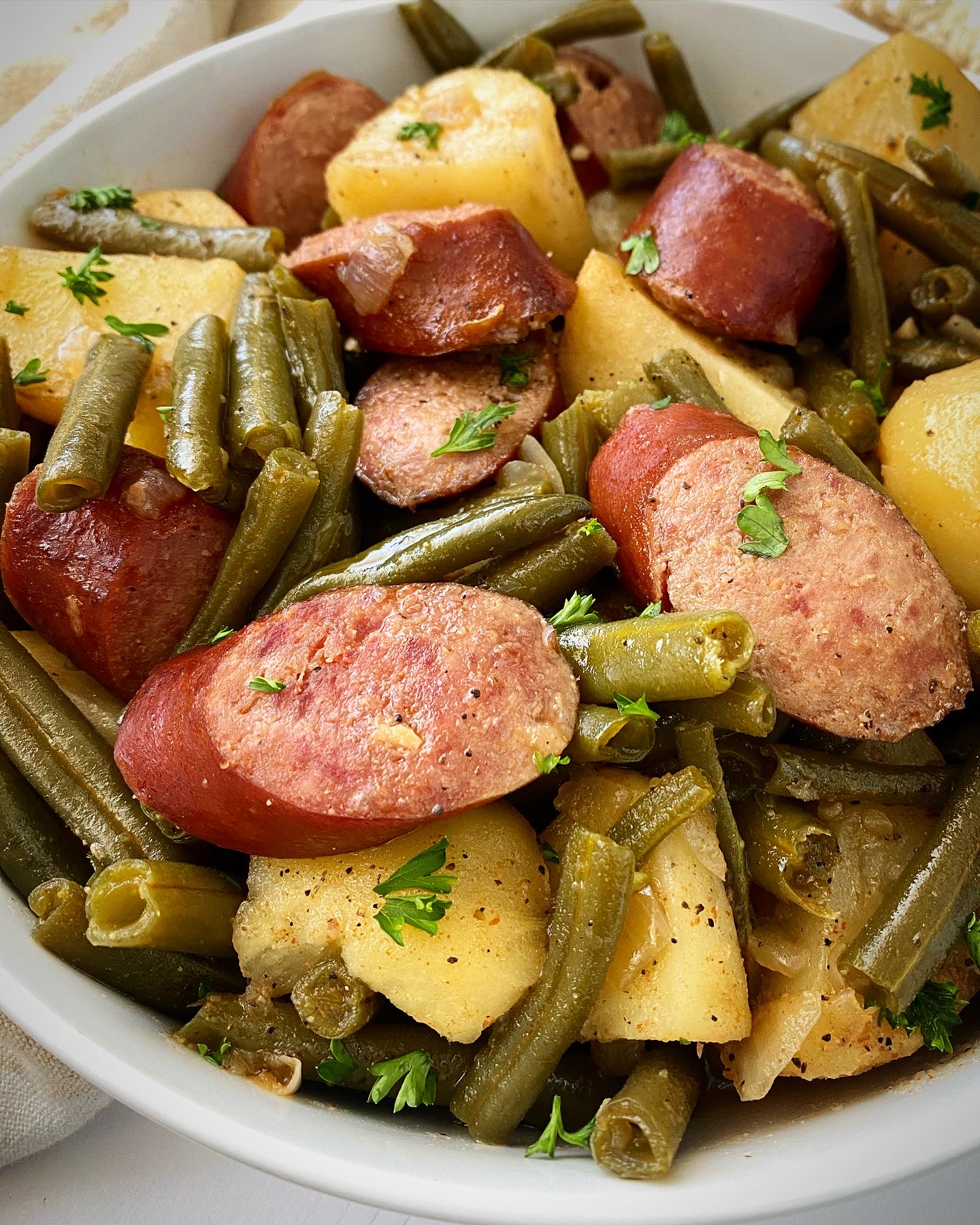 close up shot of cooked Crockpot Sausage, Potatoes Green Beans in a white bowl