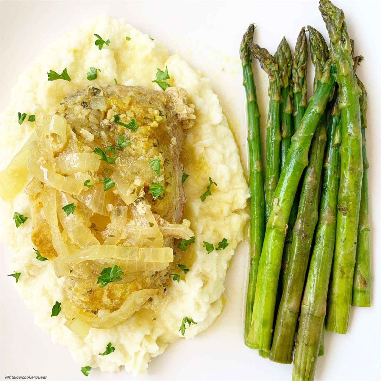Front view of onion pork chops on top of mashed cauliflower and asparagus.