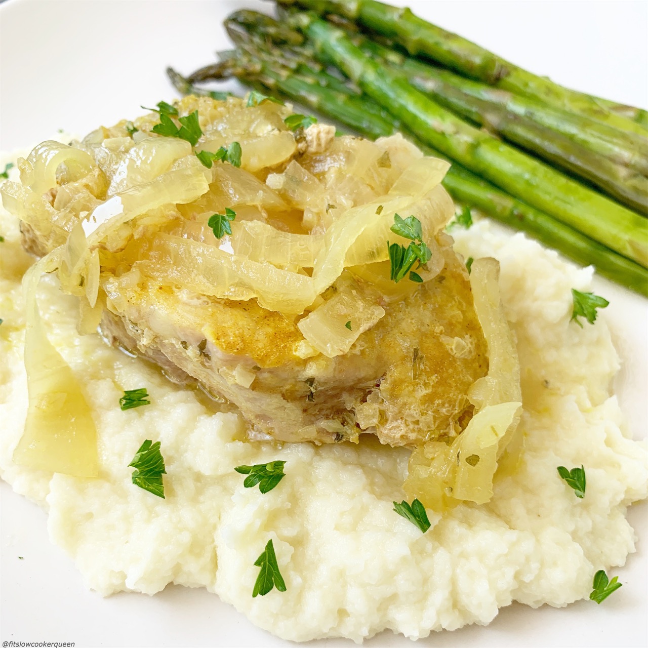 French onion pork chops on top of mashed cauliflower served with asparagus. 