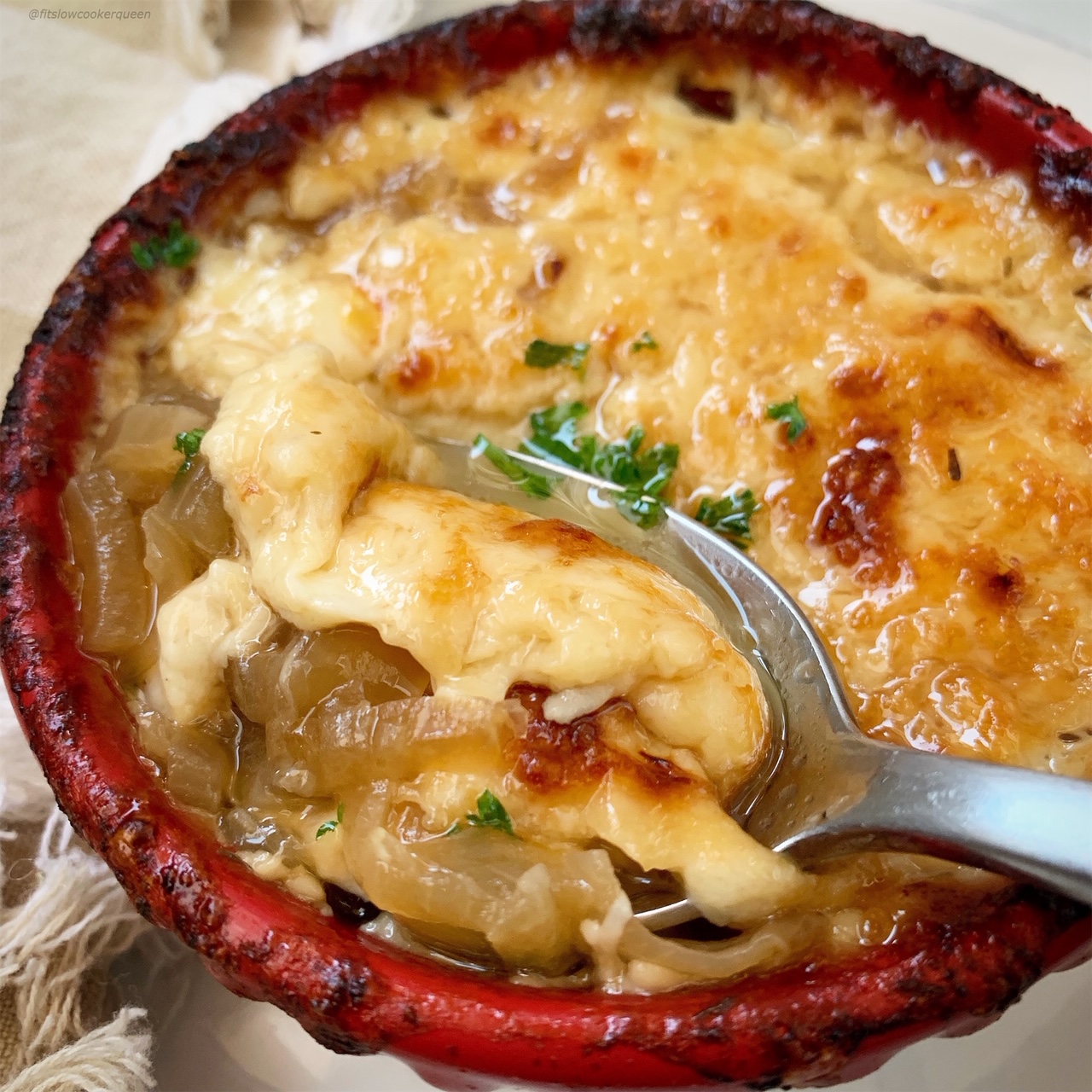 overhead shot of cooked French onion soup in a red ramkin with a silver spoon