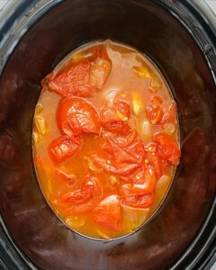 overhead shot of cooked, tomato soup in a black slow cooker unblended