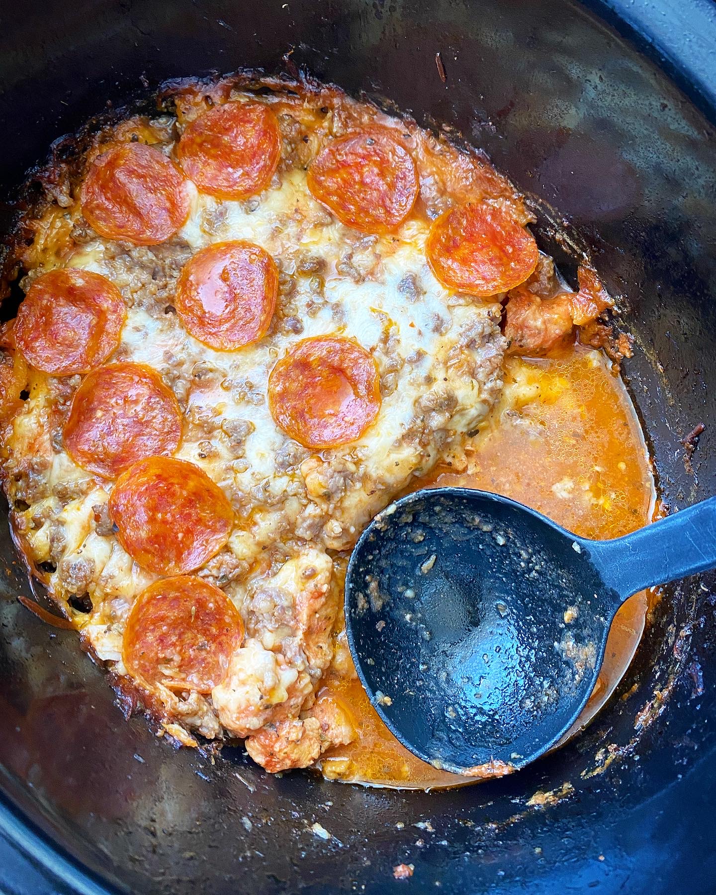 overhead shot of cooked pizza chicken in a black slow cooker with a spoonful missing