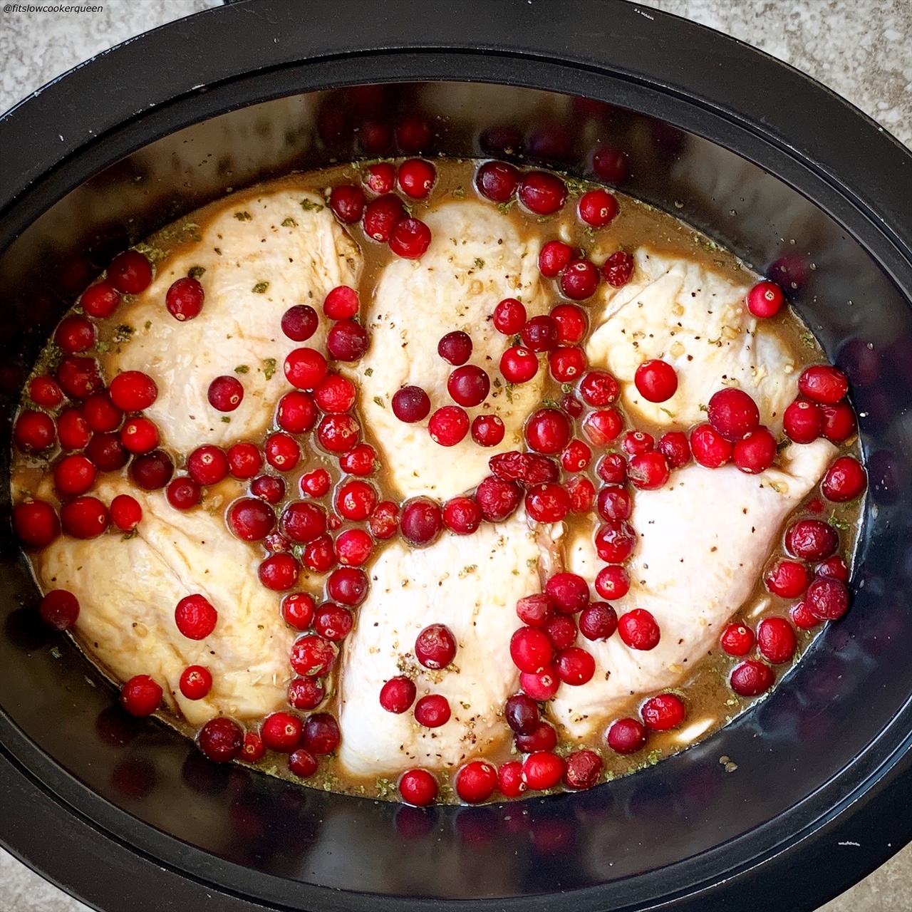 overhead shot of uncooked balsamic cranberry chicken in a black slow cooker
