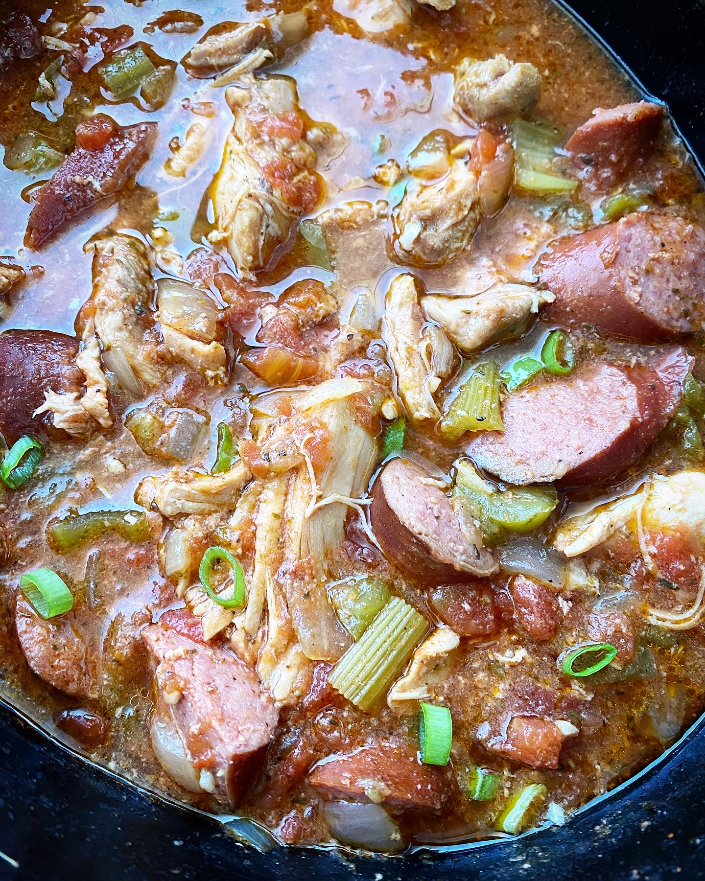 close up shot of cooked Cajun chicken & sausage in a black slow cooker