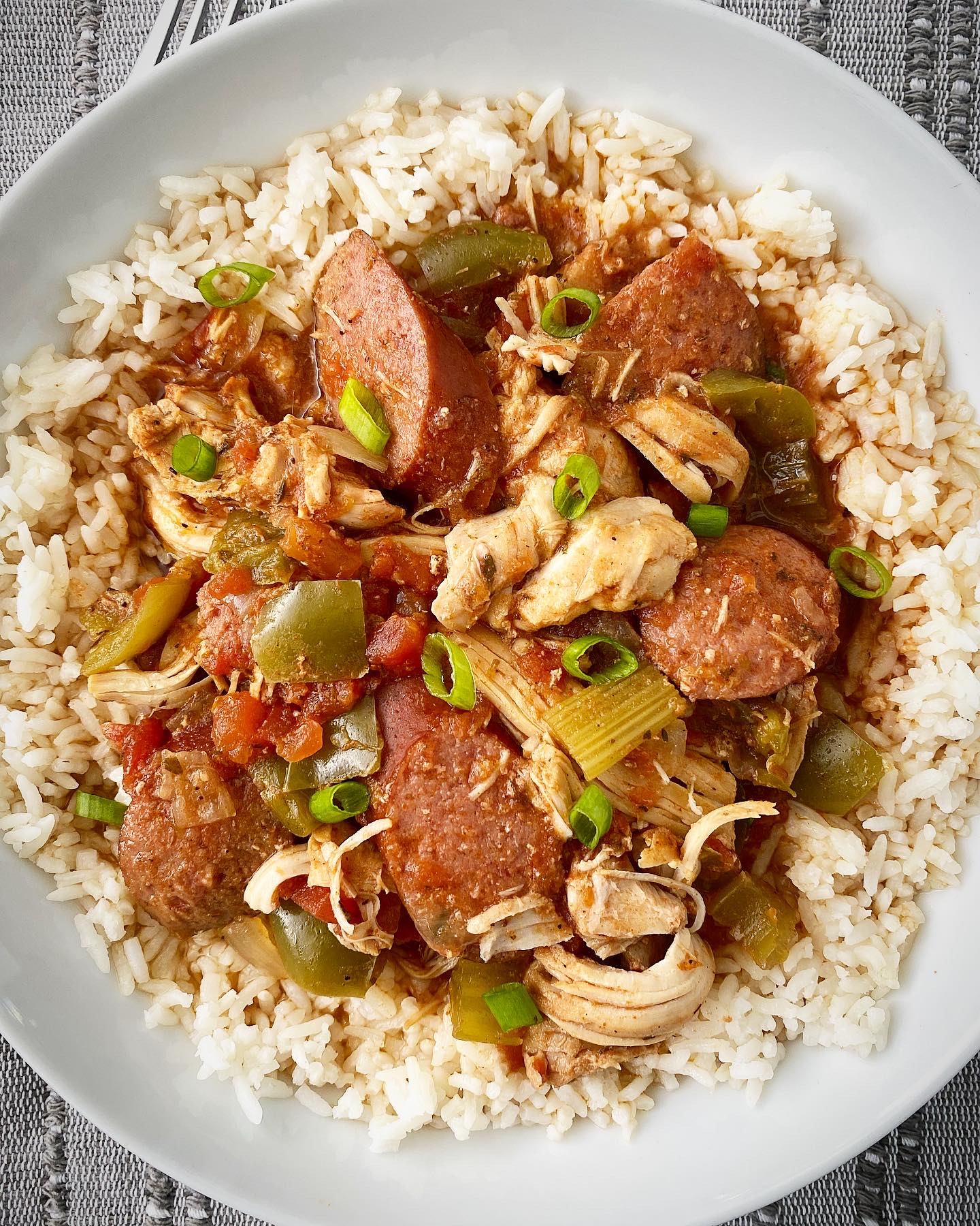 overhead shot of cooked Cajun chicken & sausage over white rice in a white bowl