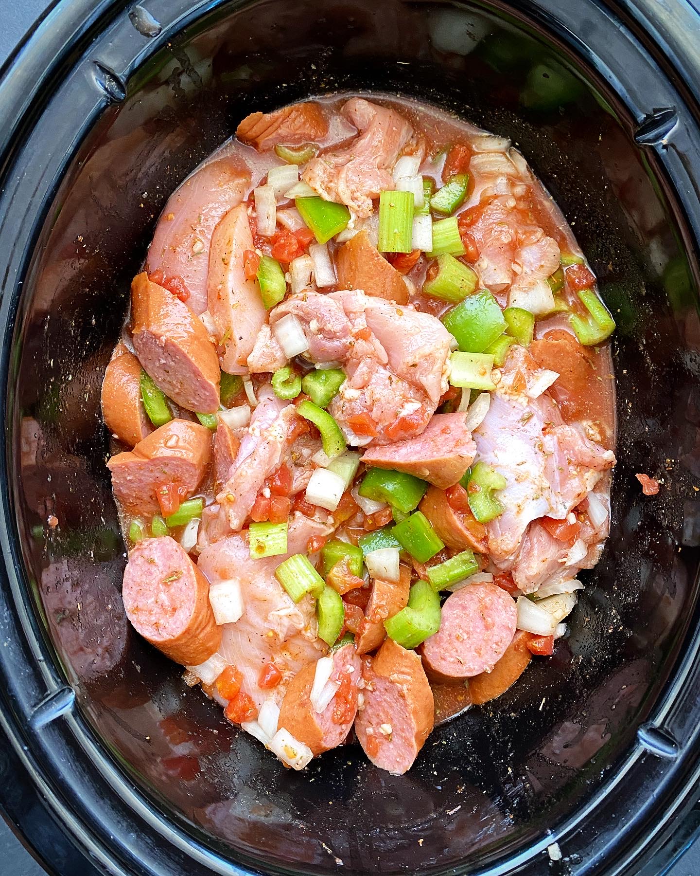 overhead shot of uncooked Cajun chicken & sausage in a black slow cooker