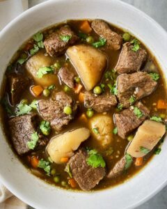 overhead shot of cilantro beef stew in a white bowl garnished with fresh cilantro