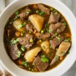 overhead shot of cilantro beef stew in a white bowl garnished with fresh cilantro