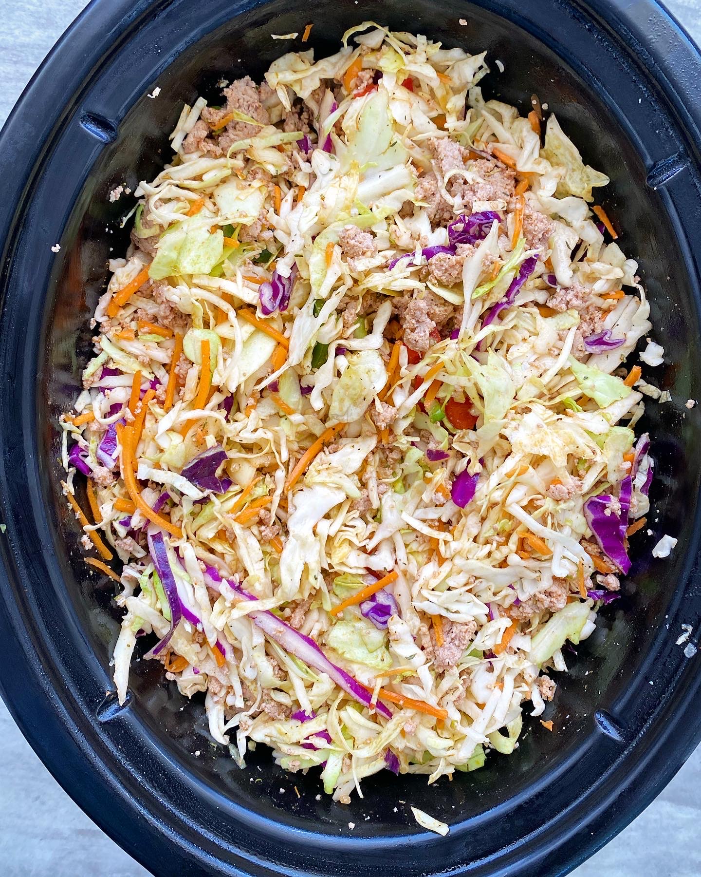 overhead shot of uncooked spicy turkey slaw in a black slow cooker