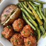overhead shot of cooked meatballs, green beans, and a baked potato in a white plate