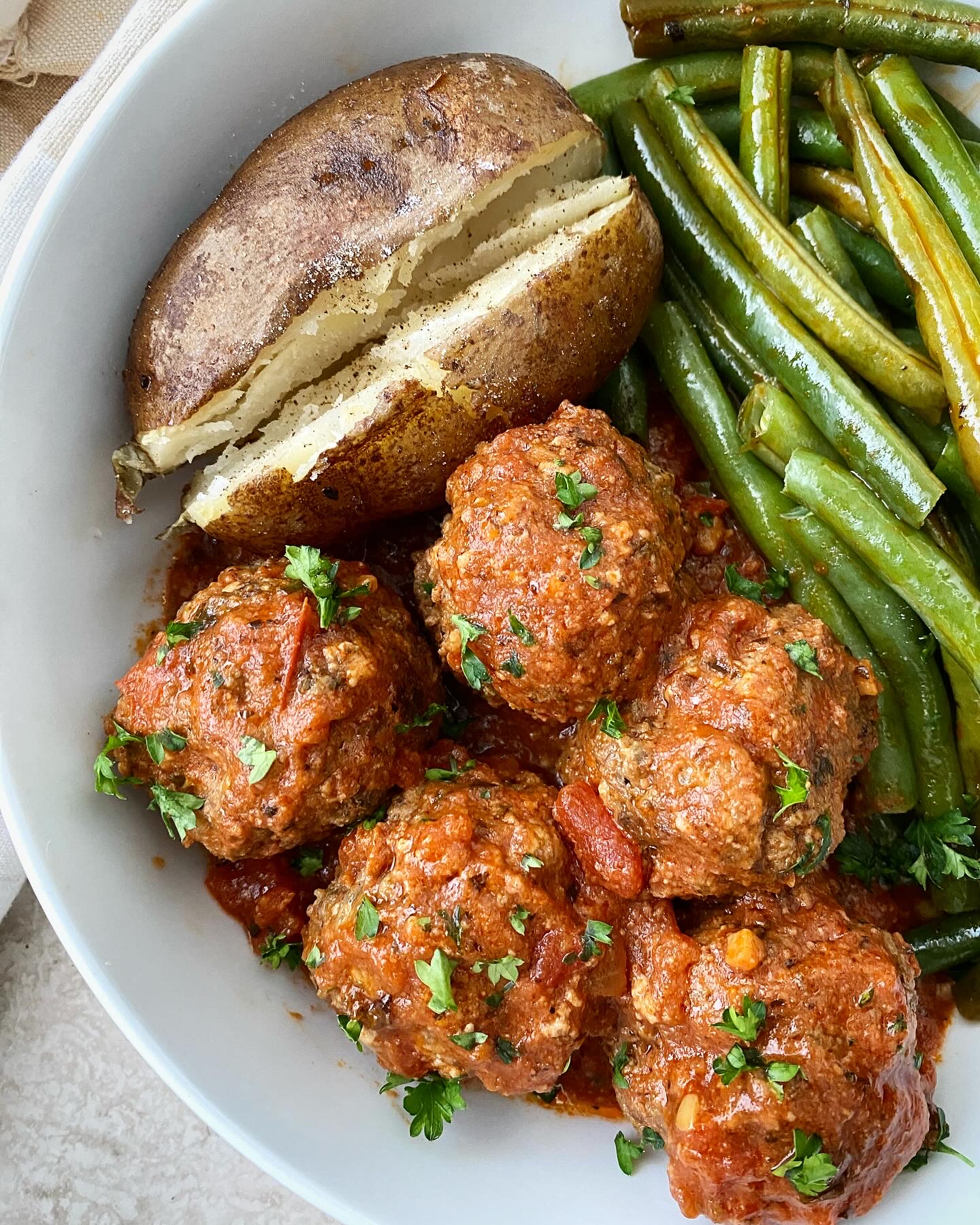 close upi shot of cooked meatballs, green beans, and a baked potato in a white plate