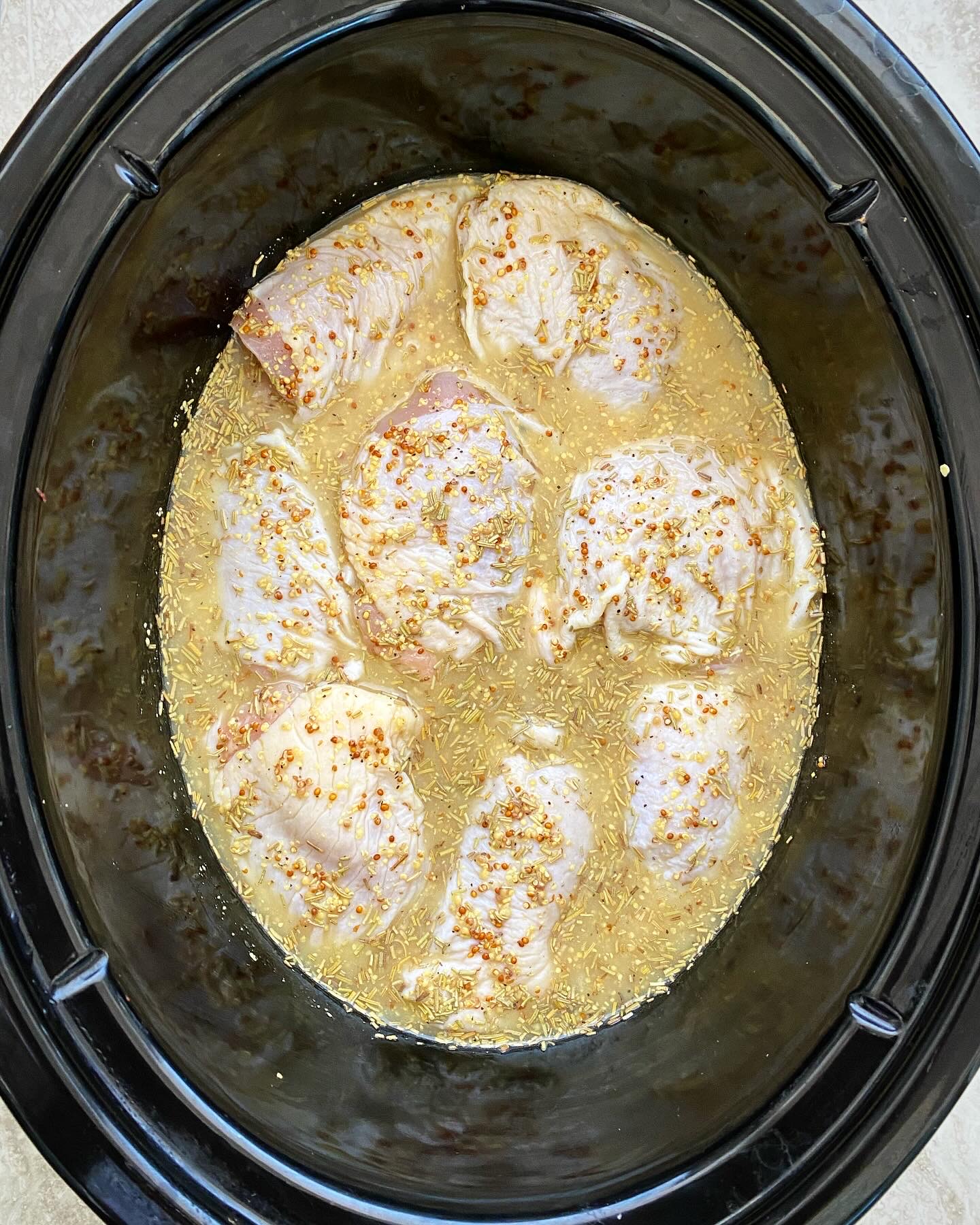 overhead shot of uncooked rosemary dijon chicken in a black slow cooker