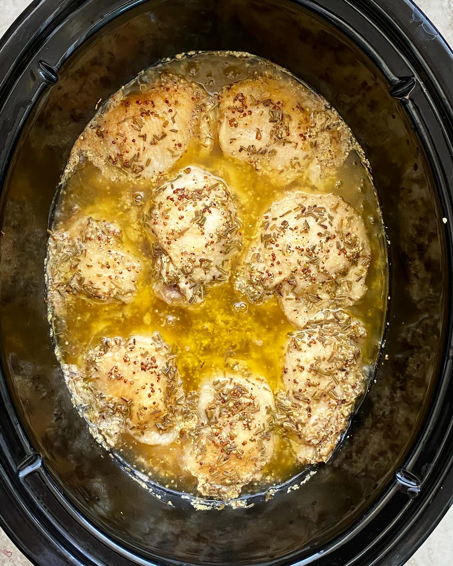 overhead shot of cooked rosemary dijon chicken in a black slow cooker
