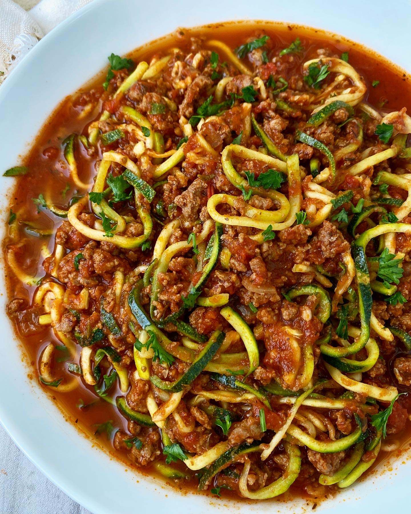 overhead side shot of cooked zoodles & meat sauce on a white plate