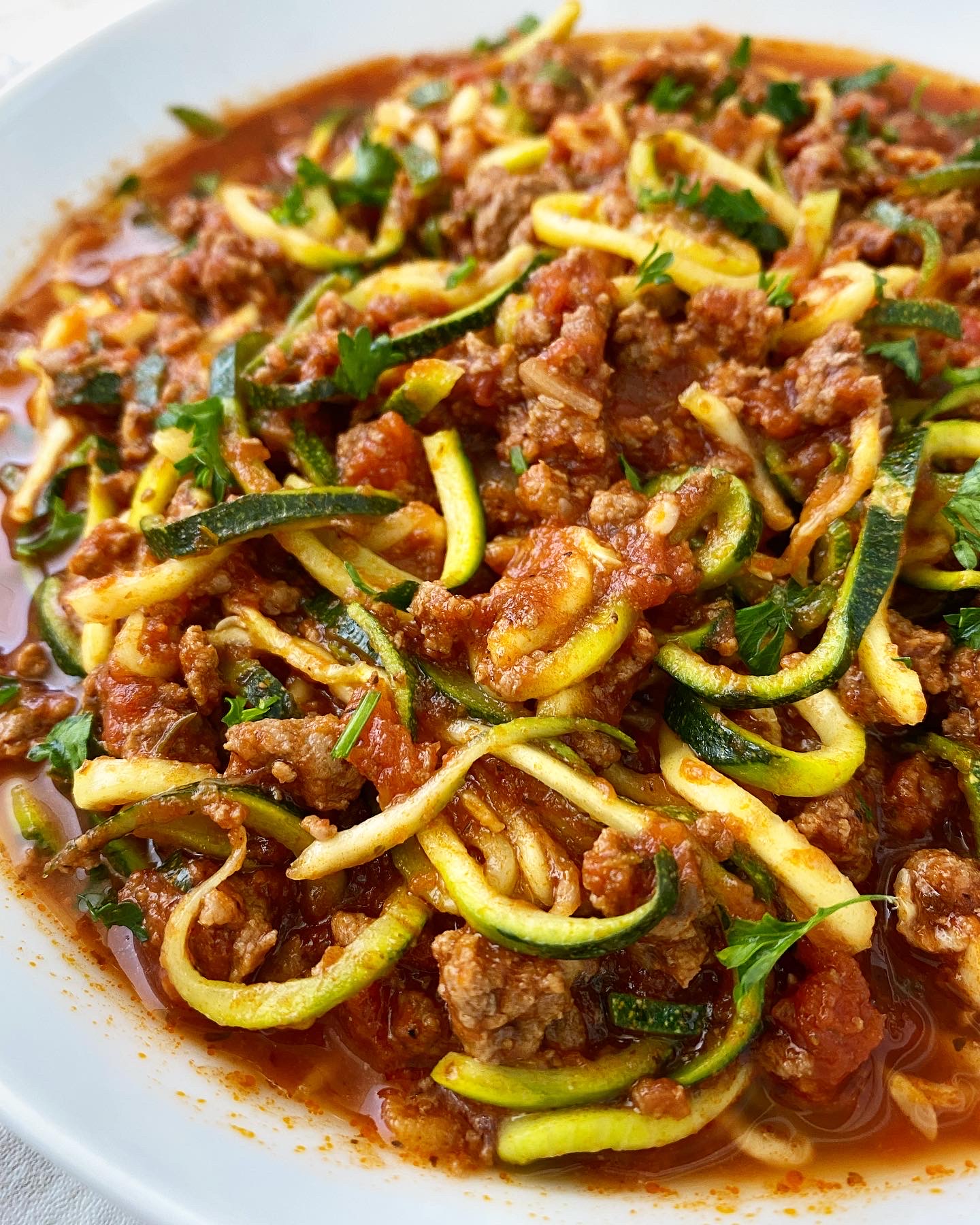 overhead side shot of cooked zoodles & meat sauce on a white plate