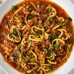 overhead shot of cooked zoodles & meat sauce on a white plate