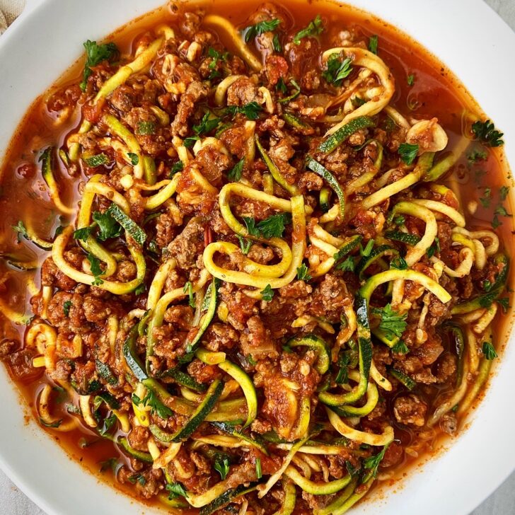 overhead shot of cooked zoodles & meat sauce on a white plate