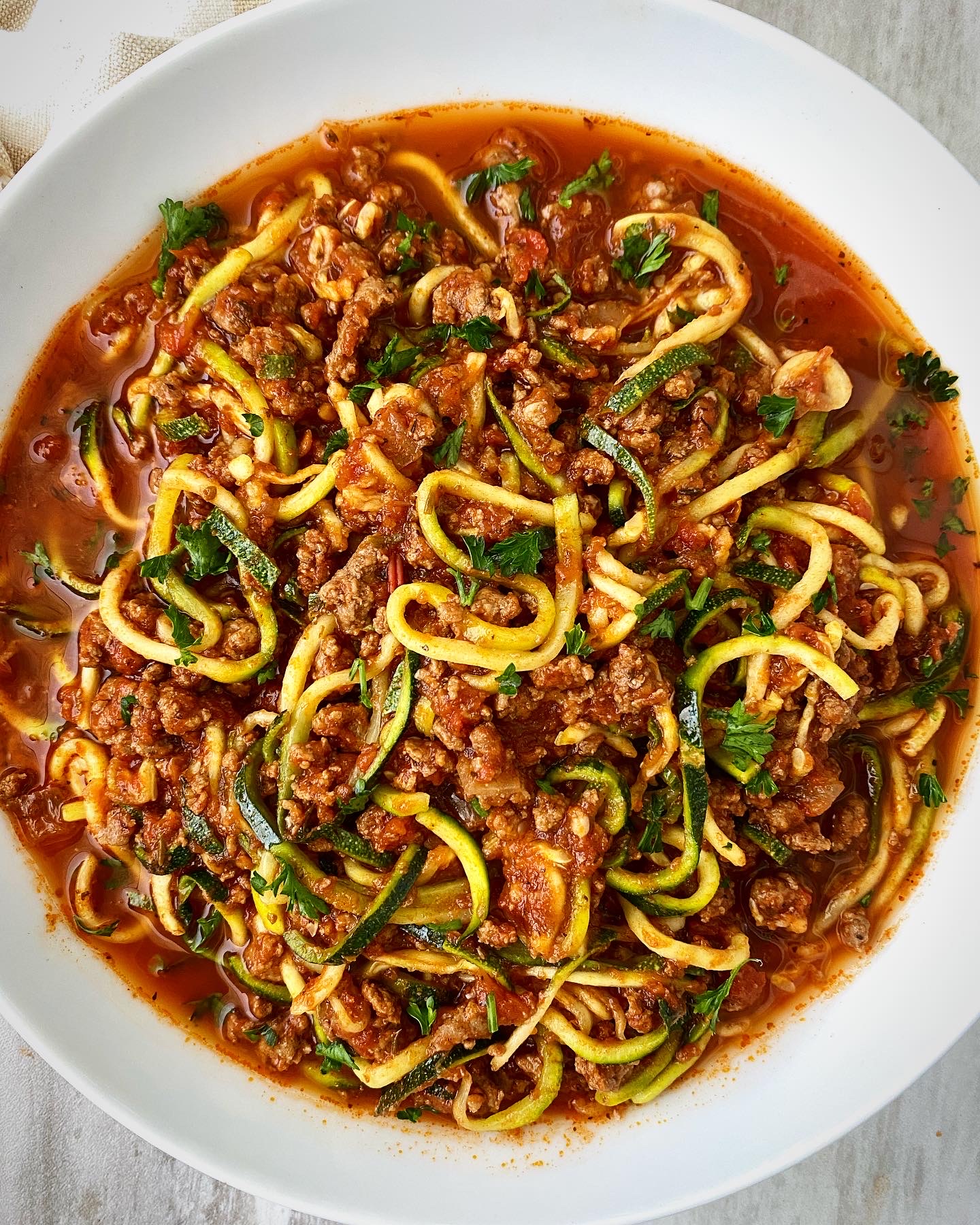 overhead shot of cooked zoodles & meat sauce on a white plate