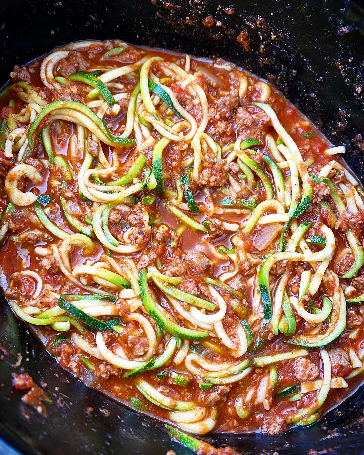 close up, side shot of meat sauce with zucchini noodles stirred in in a black slow cooker