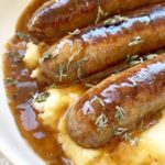 overhead shot of cooked bangers on a bed of mashed potatoes with gravy