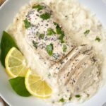 close up shot of lemon basil chicken sliced over a bed of mashed potatoes garnished with fresh basil and sliced lemon