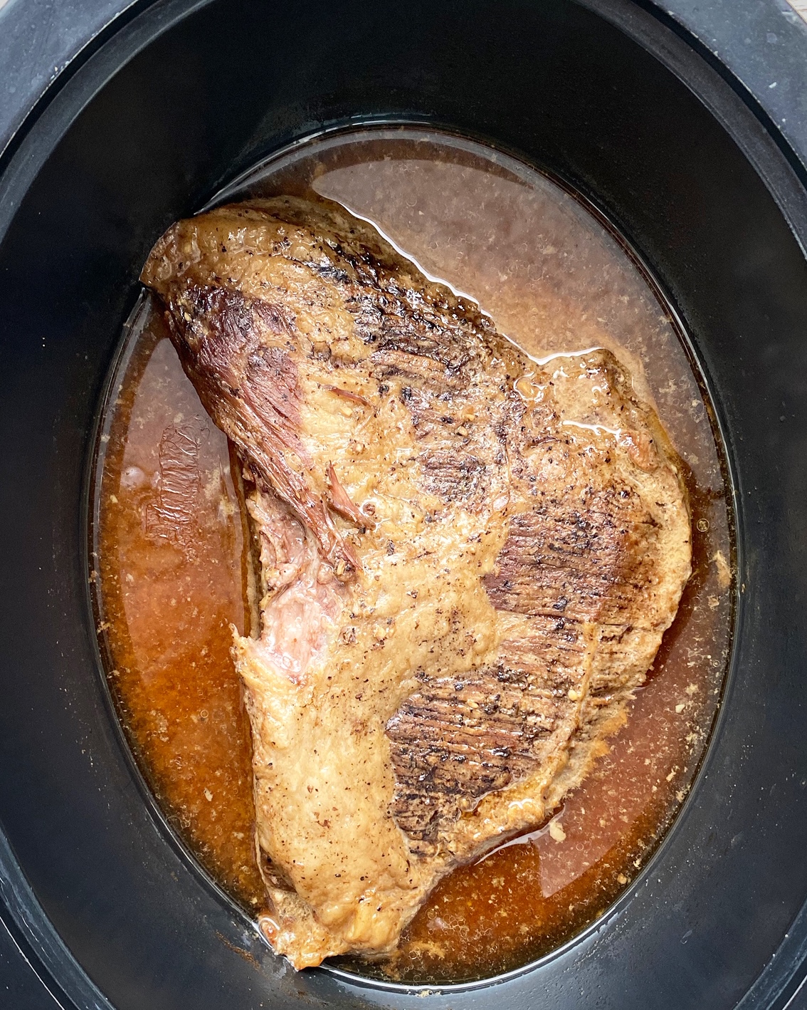 overhead shot of cooked brisket in the black slow cooker